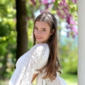 Headshot of Kristina in a white dress, posing in front of trees.