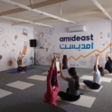 A Group Of Alumni Sitting Cross Legged On Yoga Mats With Their Hands Stretched Over Their Heads