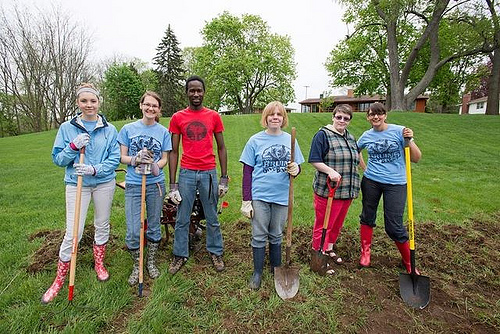 six people stand in a field with shovels