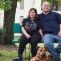 Three people sit on a bench with a dog laying on the ground in front of them