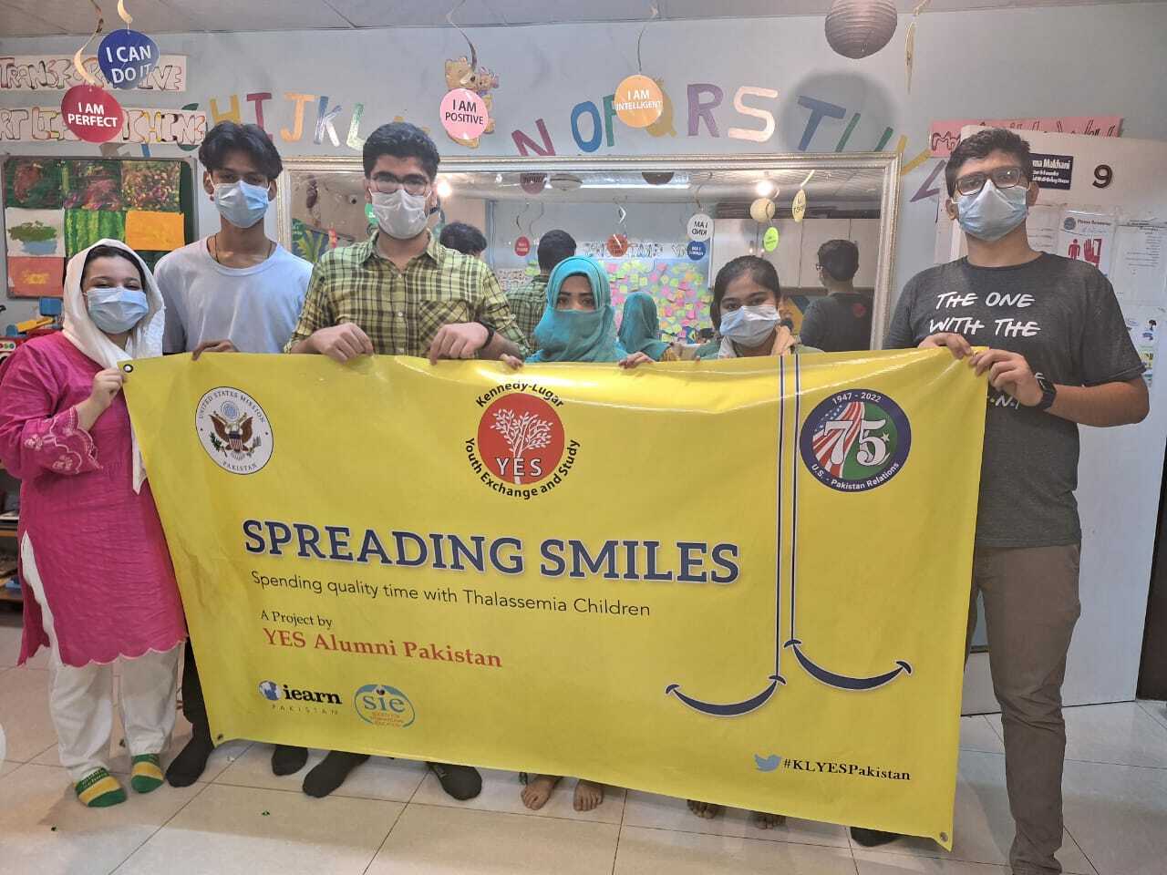 A Group Of People Pose In Front Of Banner That Reads Spreading Smiles