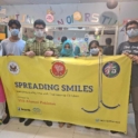A Group Of People Pose In Front Of Banner That Reads Spreading Smiles