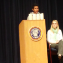 Sam Giving A Speech Behind A Podium At His School