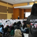 Student With A Shirt That Reads 22Alumni22 Watches A Presentation With A Group Of Other Students In An Auditorium