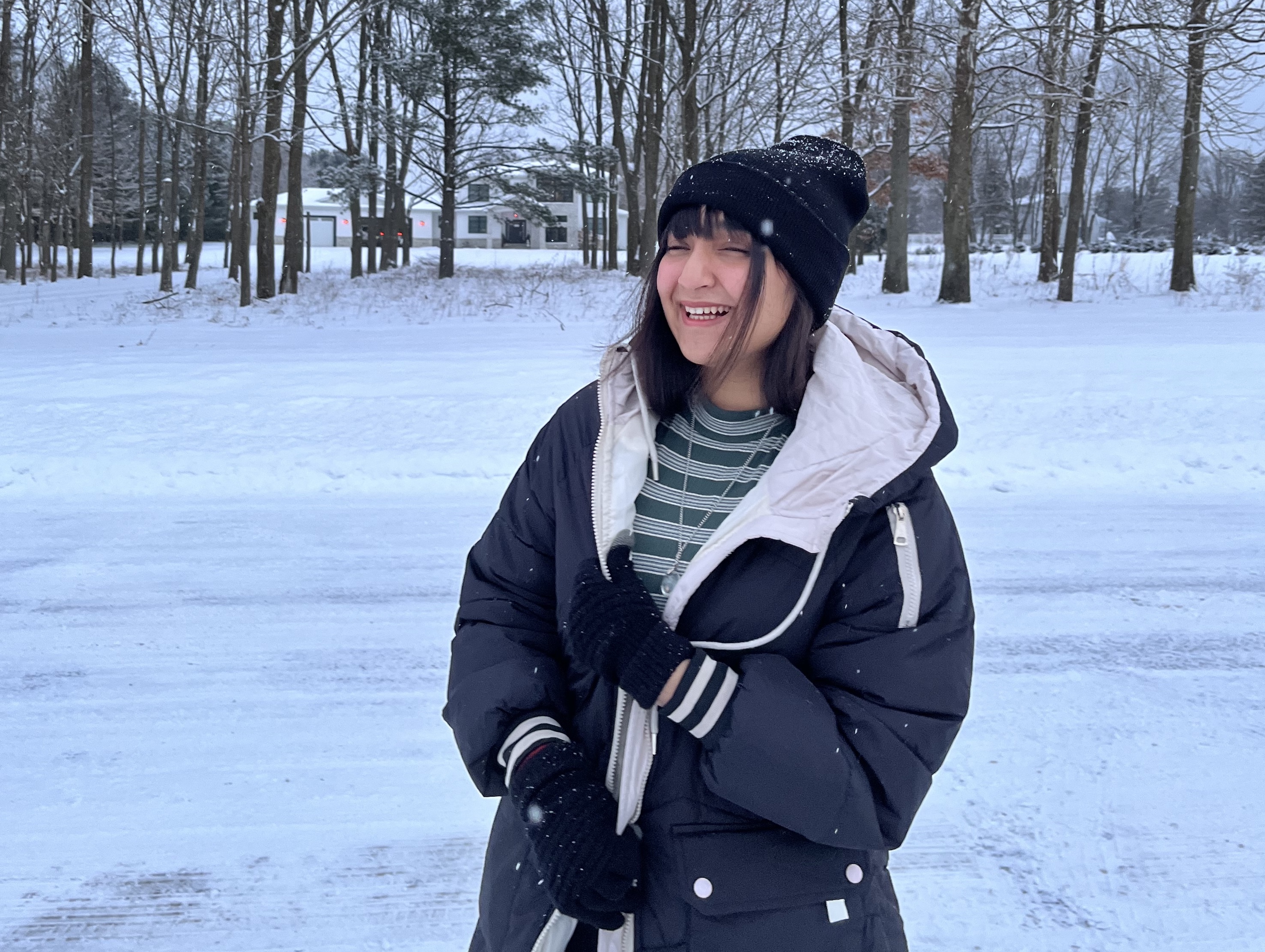 Mahnoor smiling in the snow in a winter coat, hat and gloves