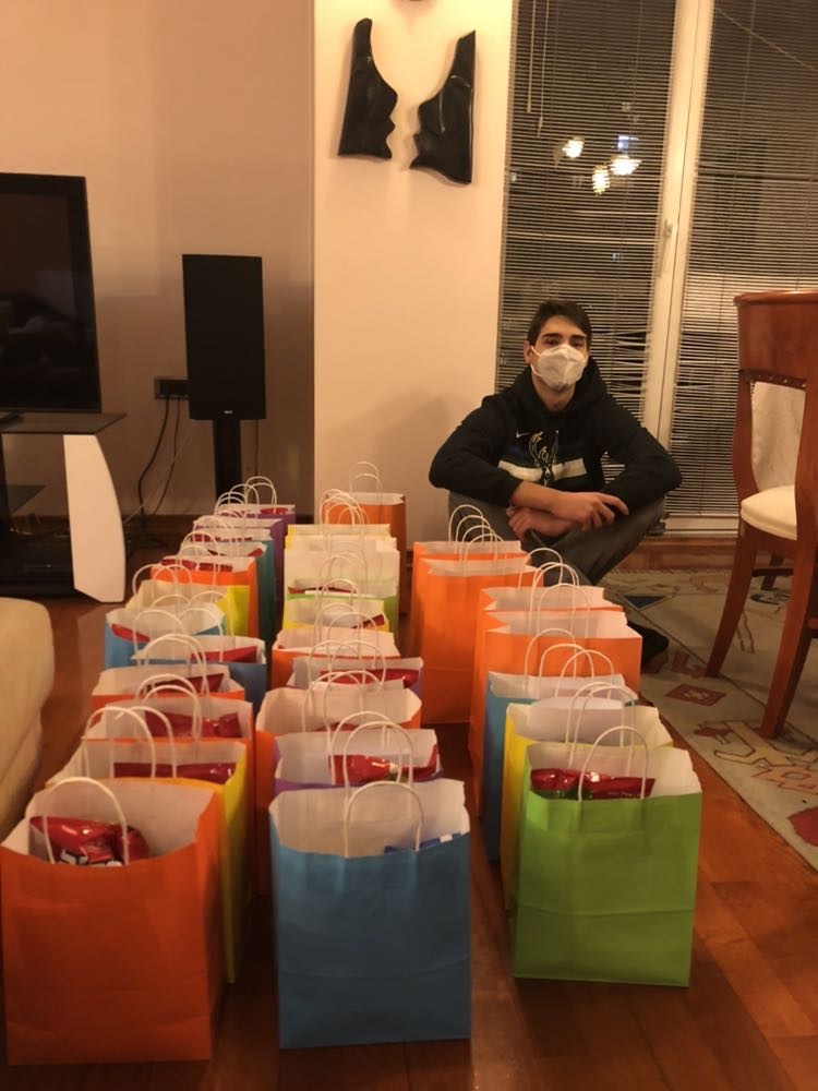 YES alumnus sits next to 30 gift bags with sweets and snacks for students with disabilities