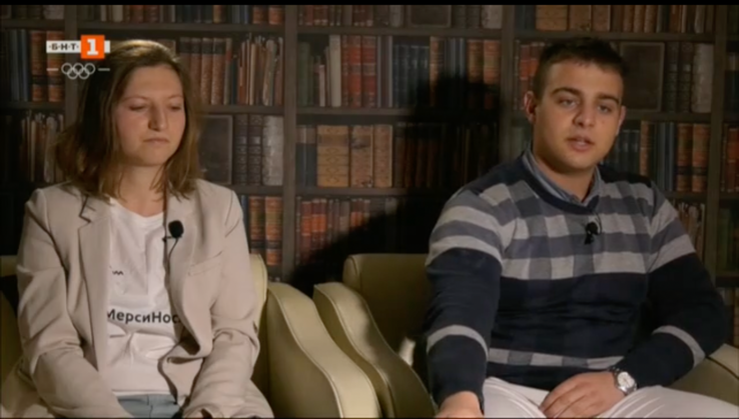 A screenshot of a TV news segment. Two people sit in a library being interviewed