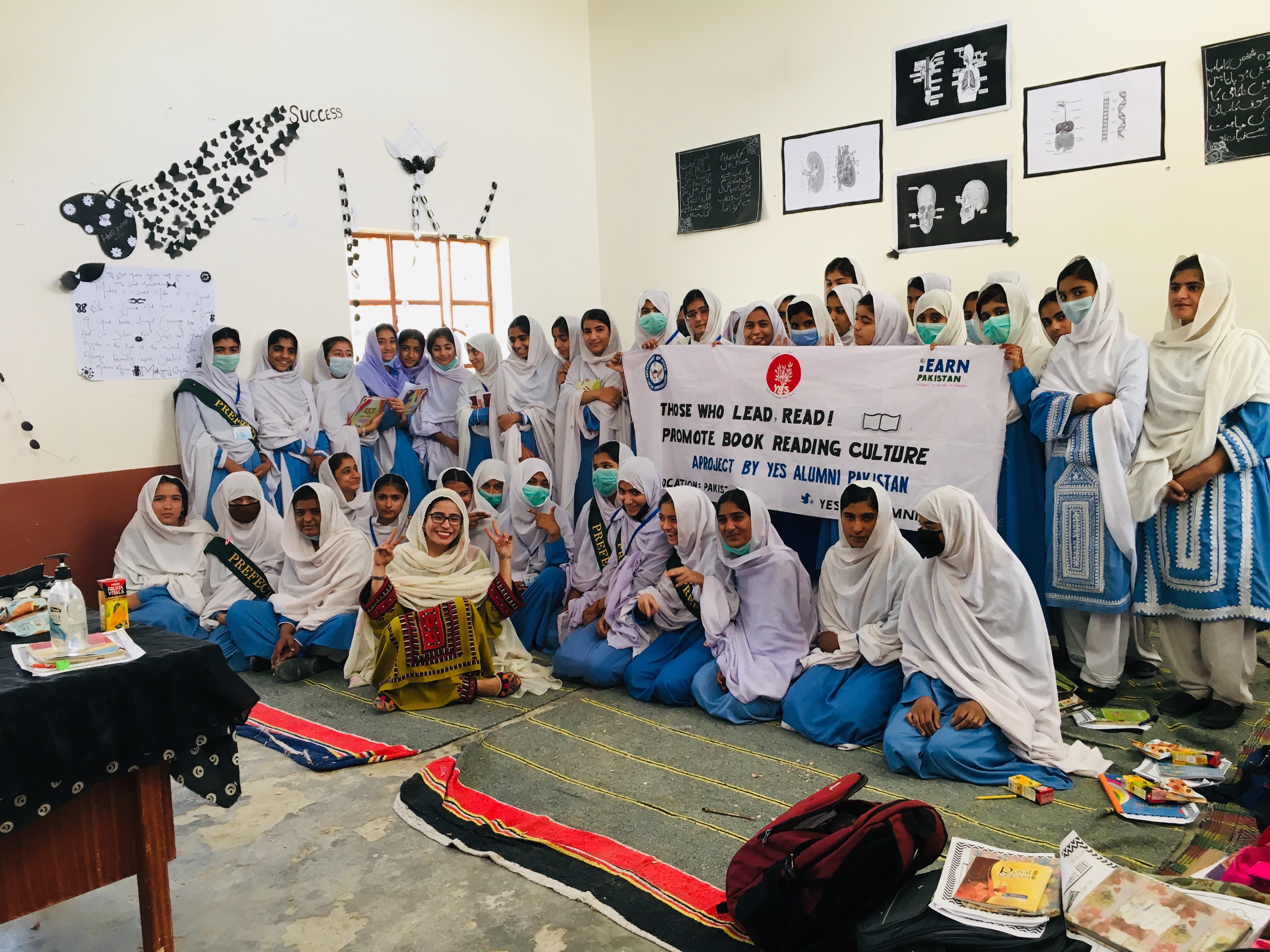 Girls from a public school sit in a classroom with some of them holding a sign that reads "Those who read. Lead!"