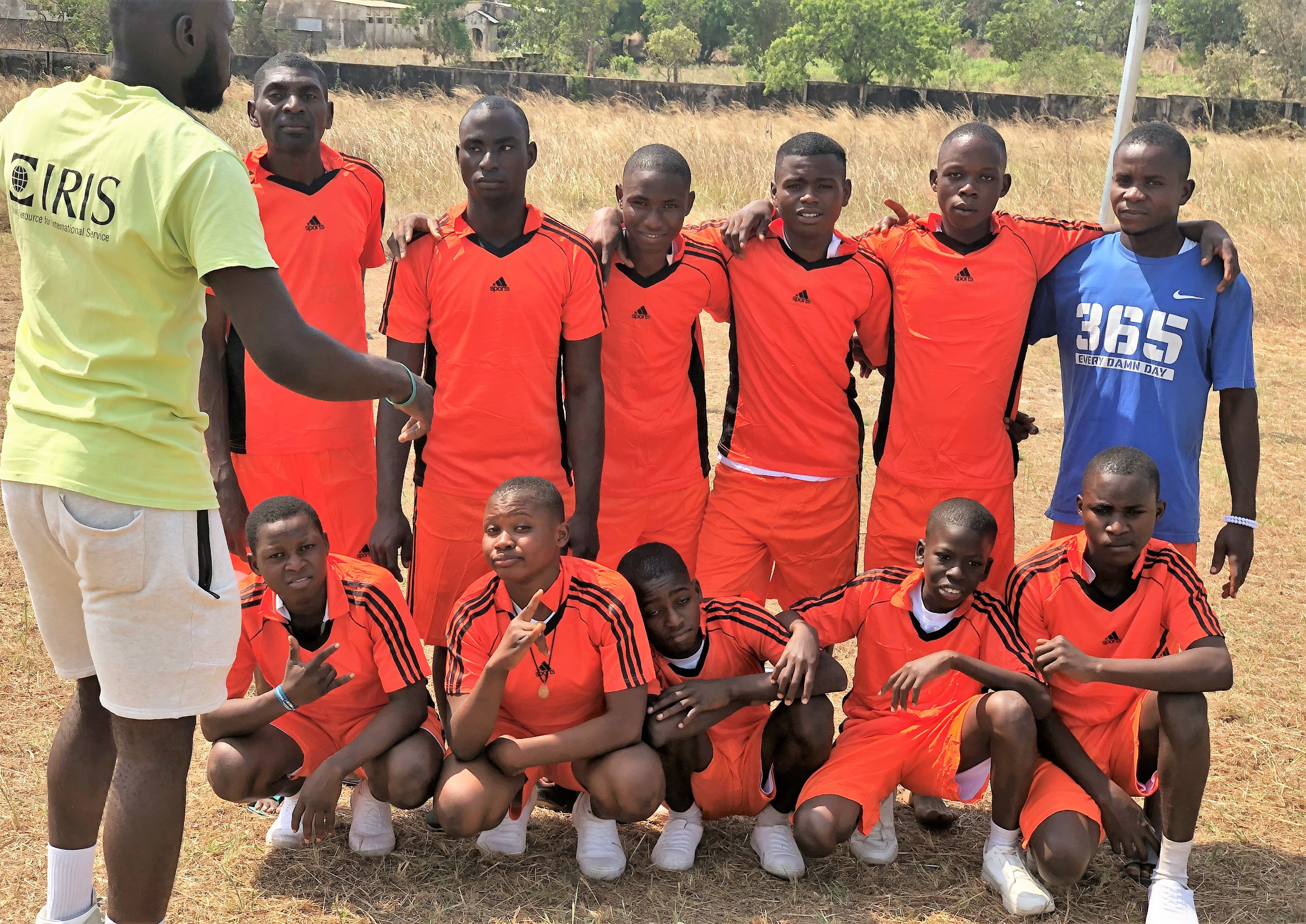A soccer team in Tanzania wearing red uniforms, a coach in an IRIS tshirt