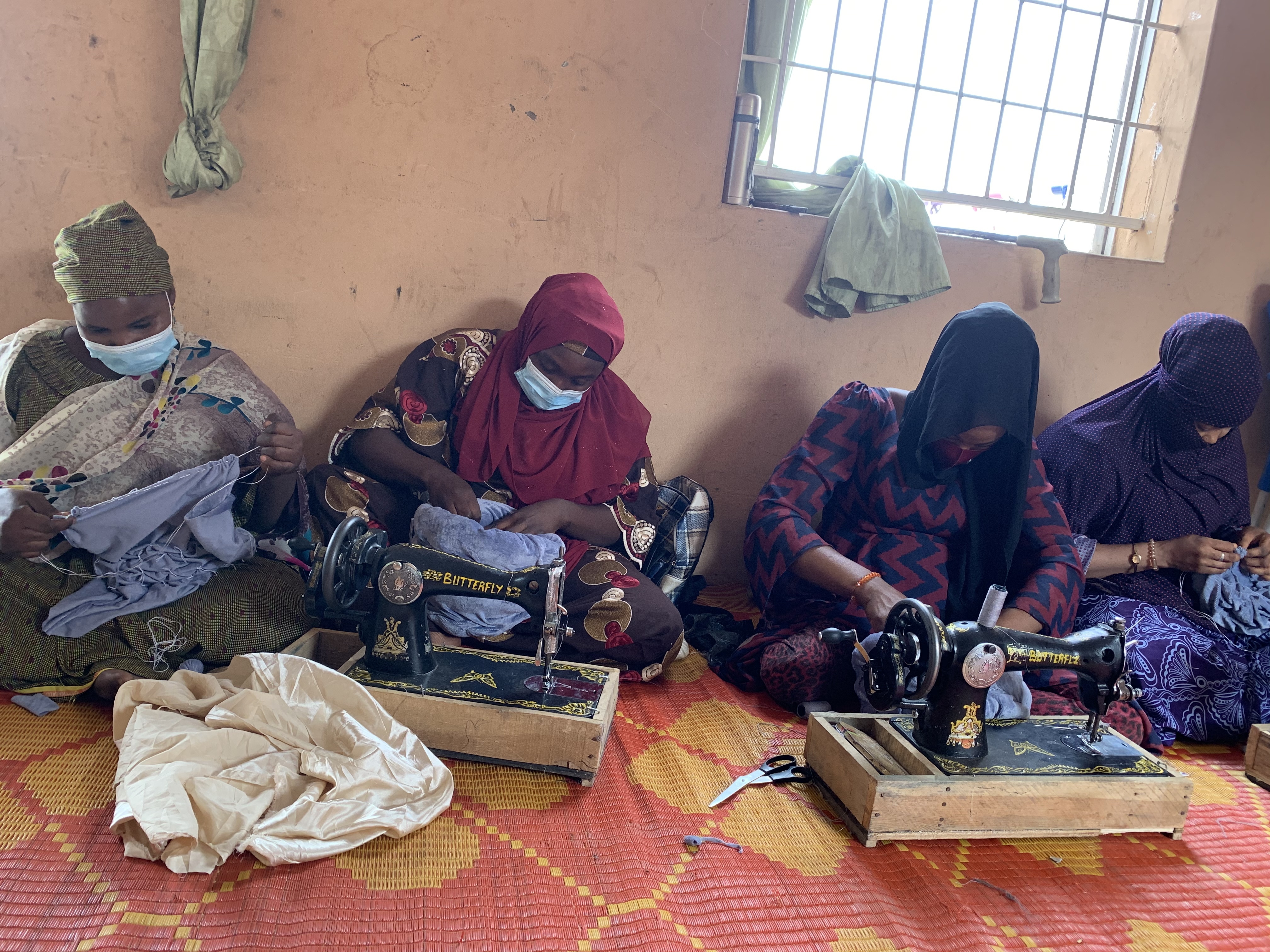 Four women sit on the ground with sewing machines