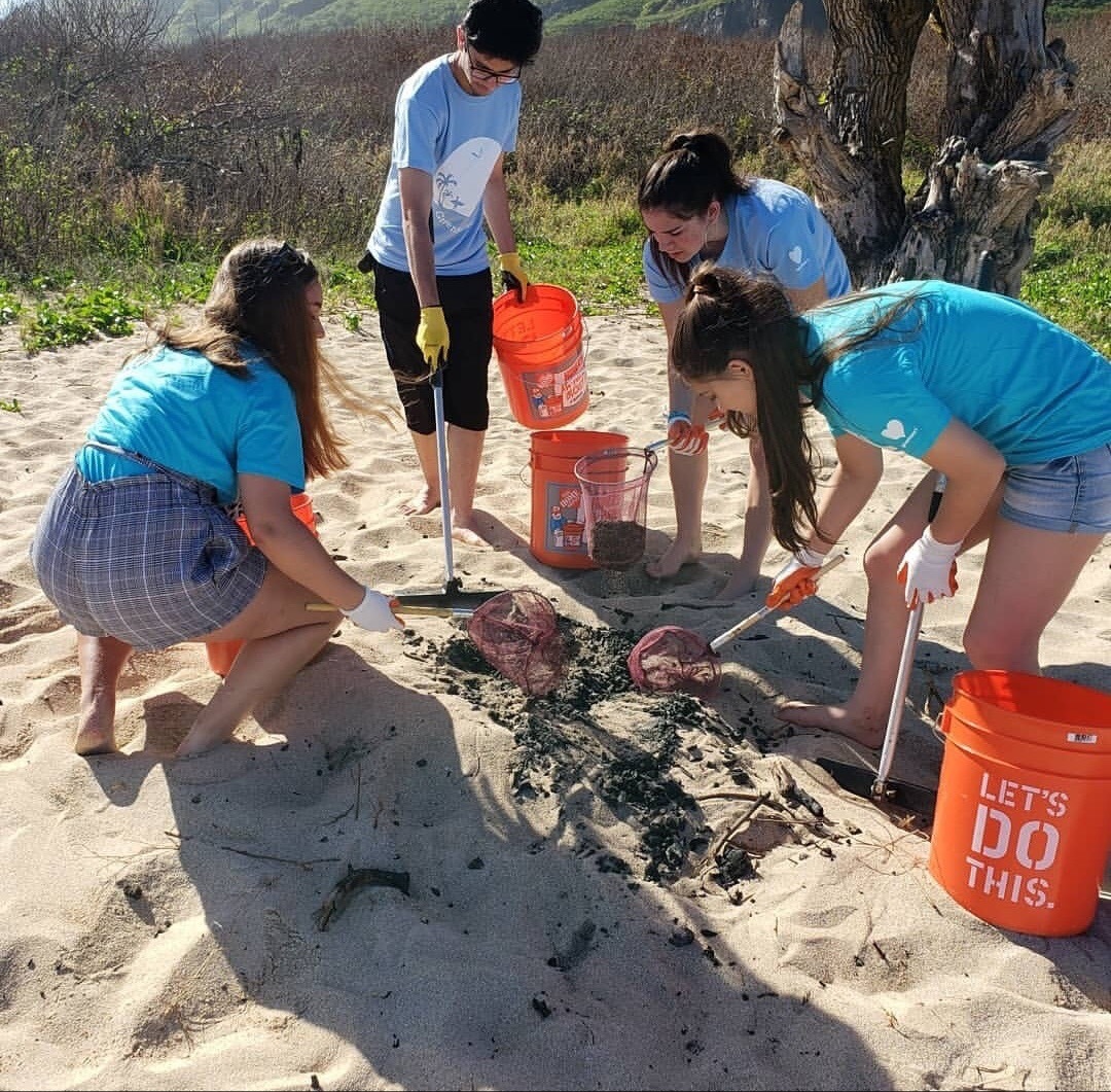 Students clean up a beach with tools to clean up trash and orange buckets