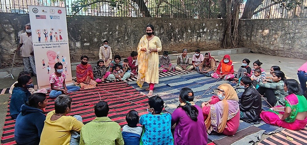 A Female Trainer Speaks To A Group Of Participants Sitting On The Ground In A Circle