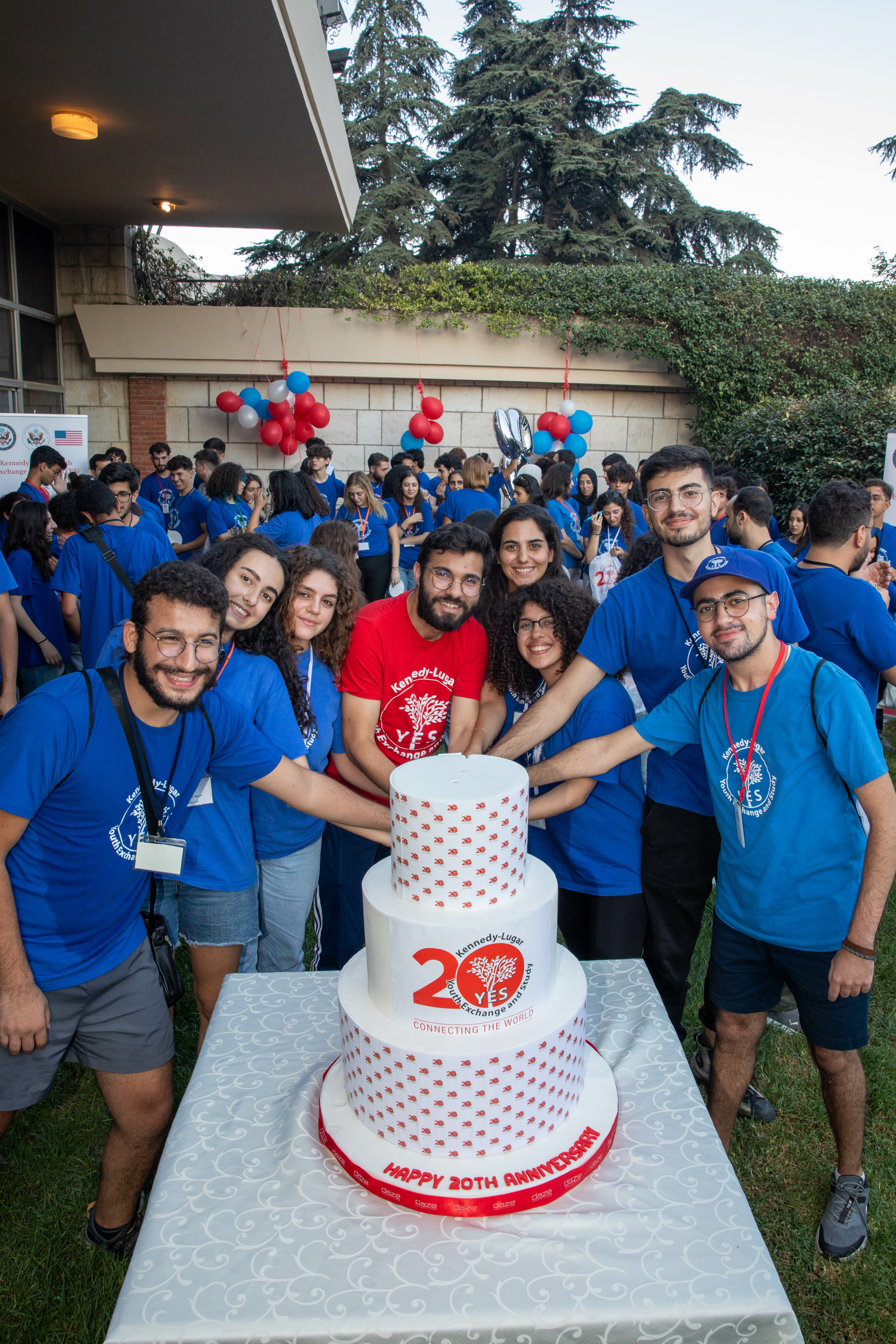 A Group Of Alumni Cutting A Cake With The 20Th Anniversary Logo