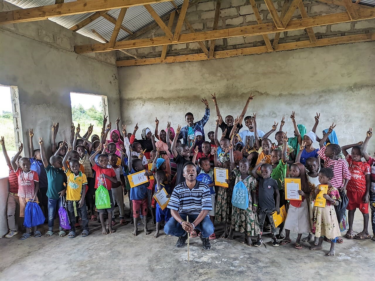 A Large Group Of Children Who Were Beneficiaries Of A Fundraiser Look Happy And Have Their Arms In The Air In Tanzania