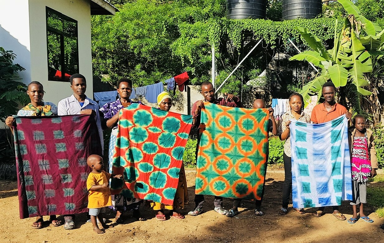 A Line Of People Hold Up Pieces Of Cloth That Have Been Tie Dyed With Batik Patterns