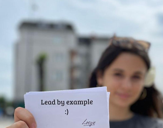 A Person Holds Up A Card That Says Lead By Example In Kosovo