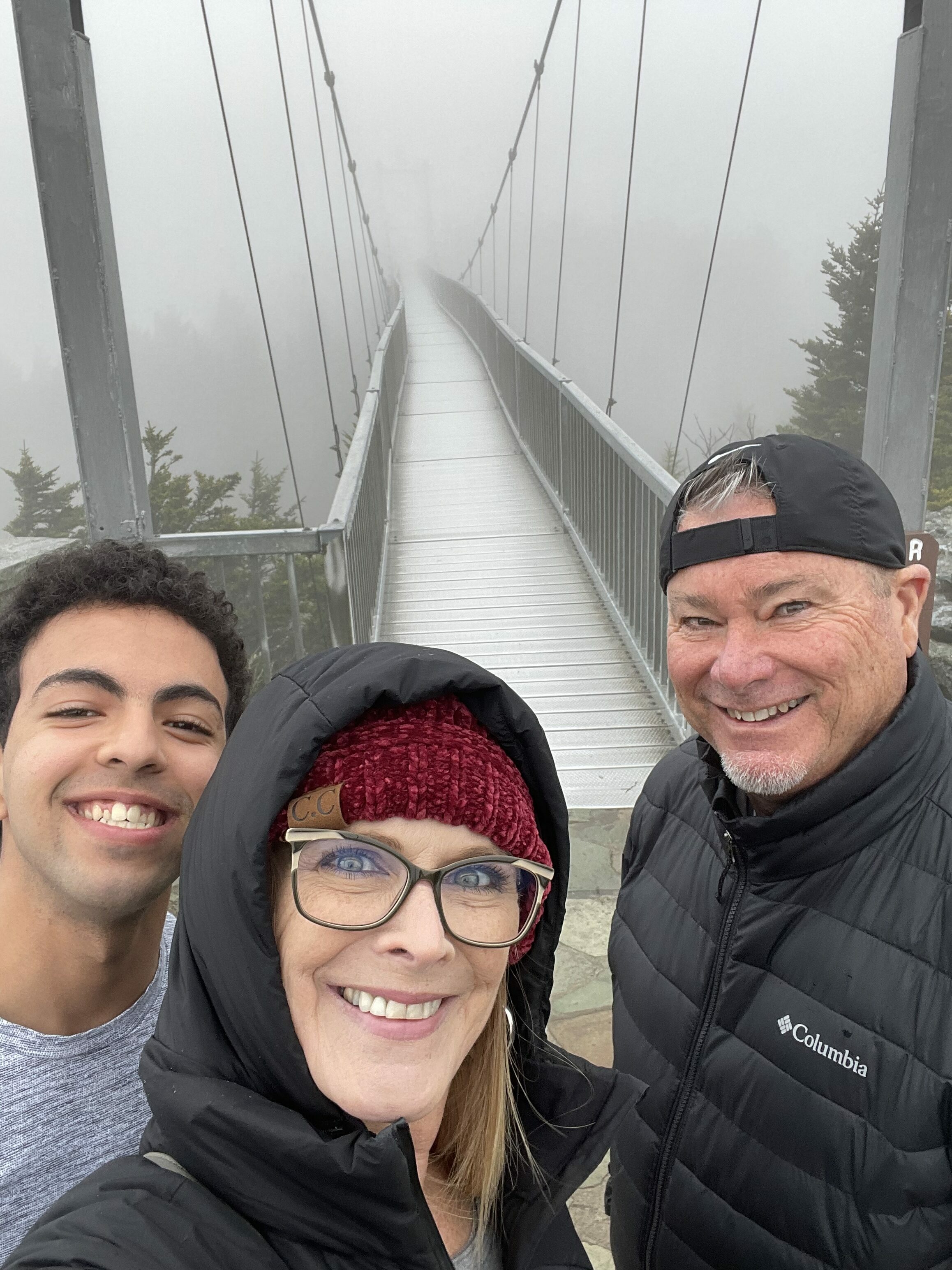 Ahmad and his host mom and dad stand in front of a suspended bridge for a selfie