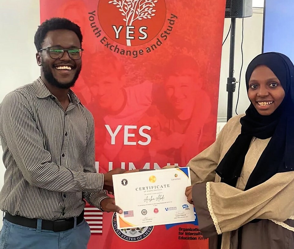 Alex Mwakilau Is Presenting A Certificate To A Participant In Front A Yes Banner