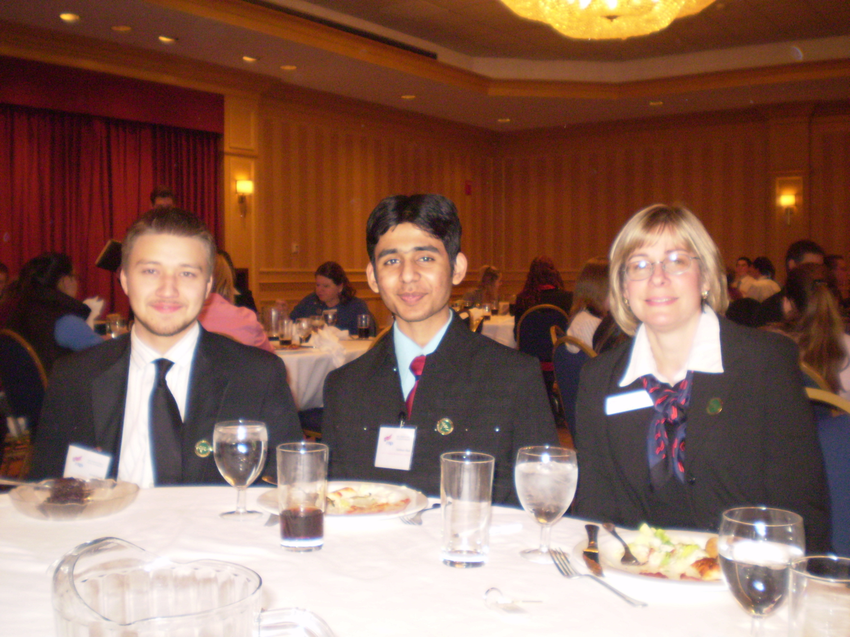 Alum Posing With Teacher And Fellow Student In Formal Wear At A Table