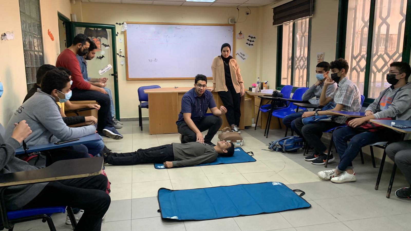 Participants in a classroom with an instructor on the floor with a participant demonstrating a first aid technique. 