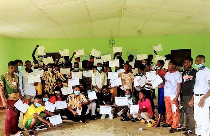 a large group of people stand in a green classroom with their certificates in the air