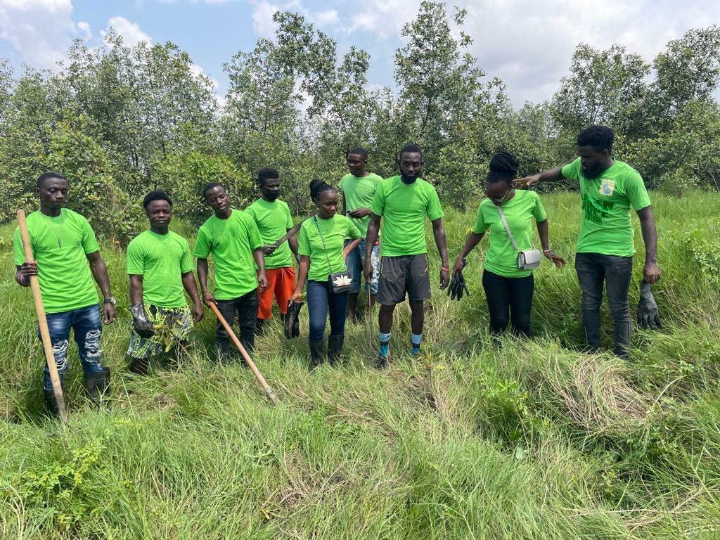 Group Of People In Green Shirts Pose Surrounded By Wetlands