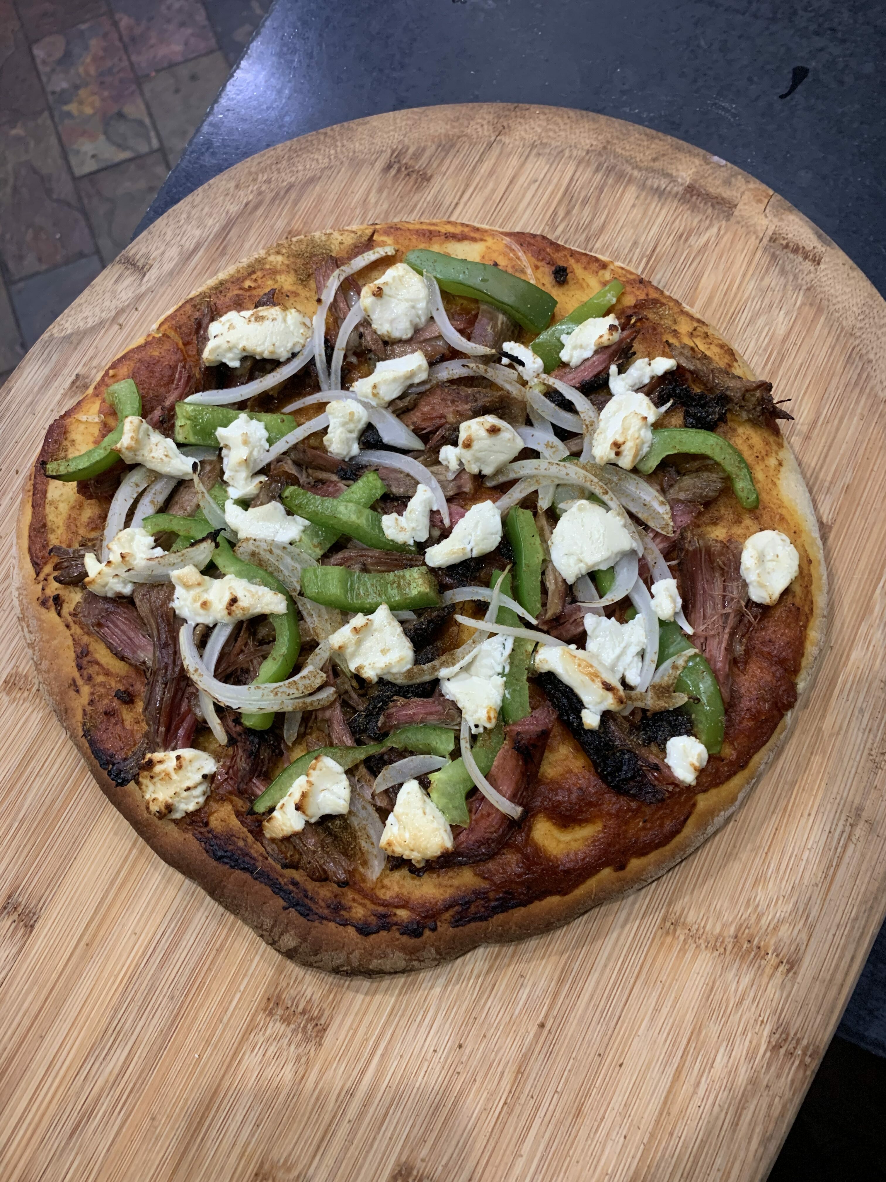 A pizza with many Moroccan ingredients sits atop a wooden cutting board