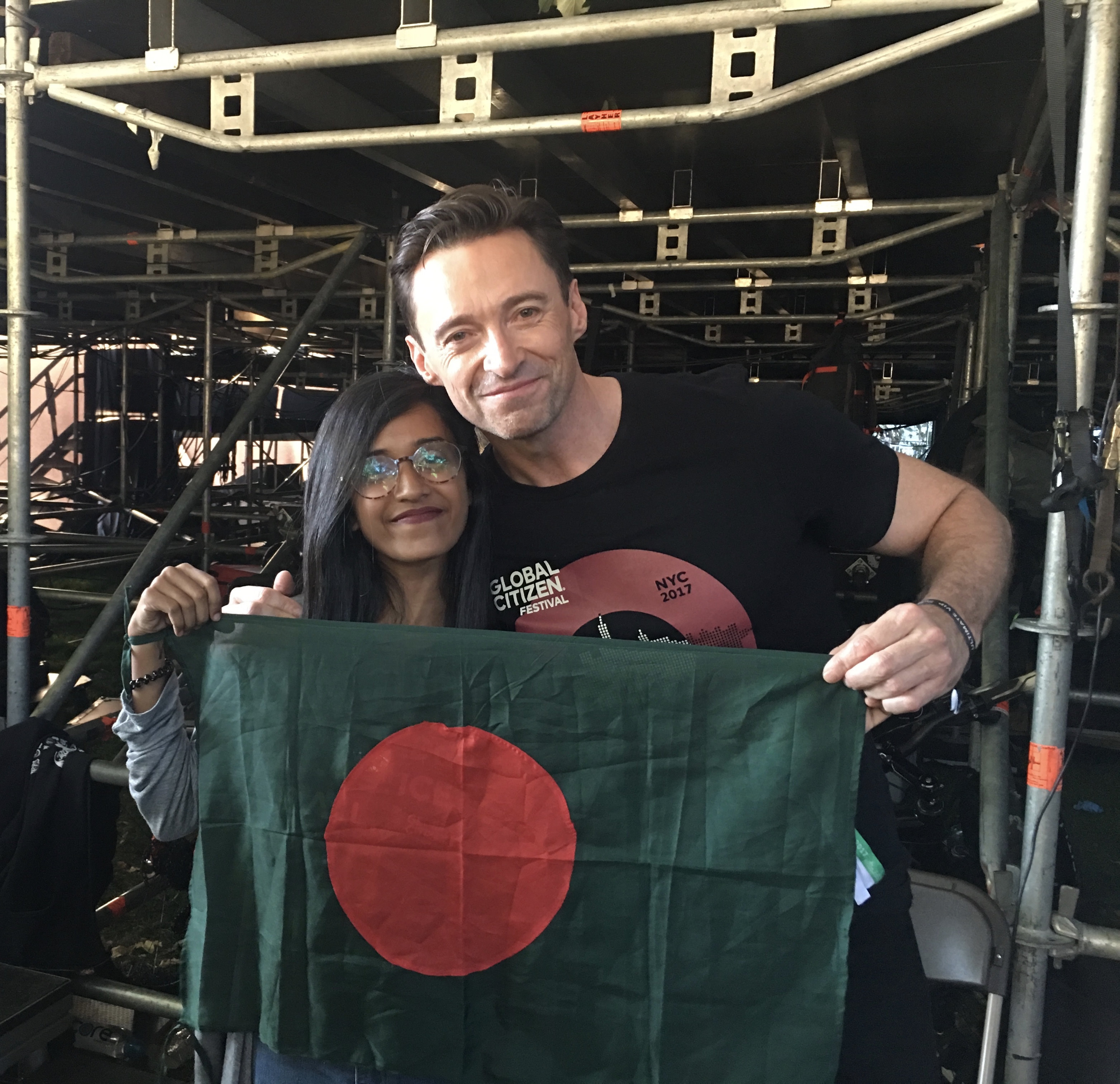 Shomy standing next to Hugh Jackman holding the Bangladeshi flag