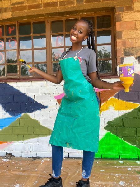 A YES alumna is holding paintbrushes and facing the camera smiling