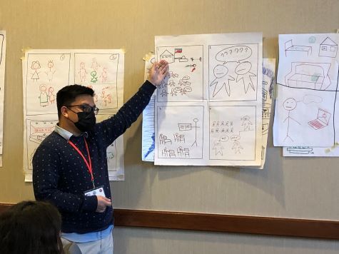Jamil wearing a mask and pointing to a storyboard drawn on paper and on a bulletin board next to him. 