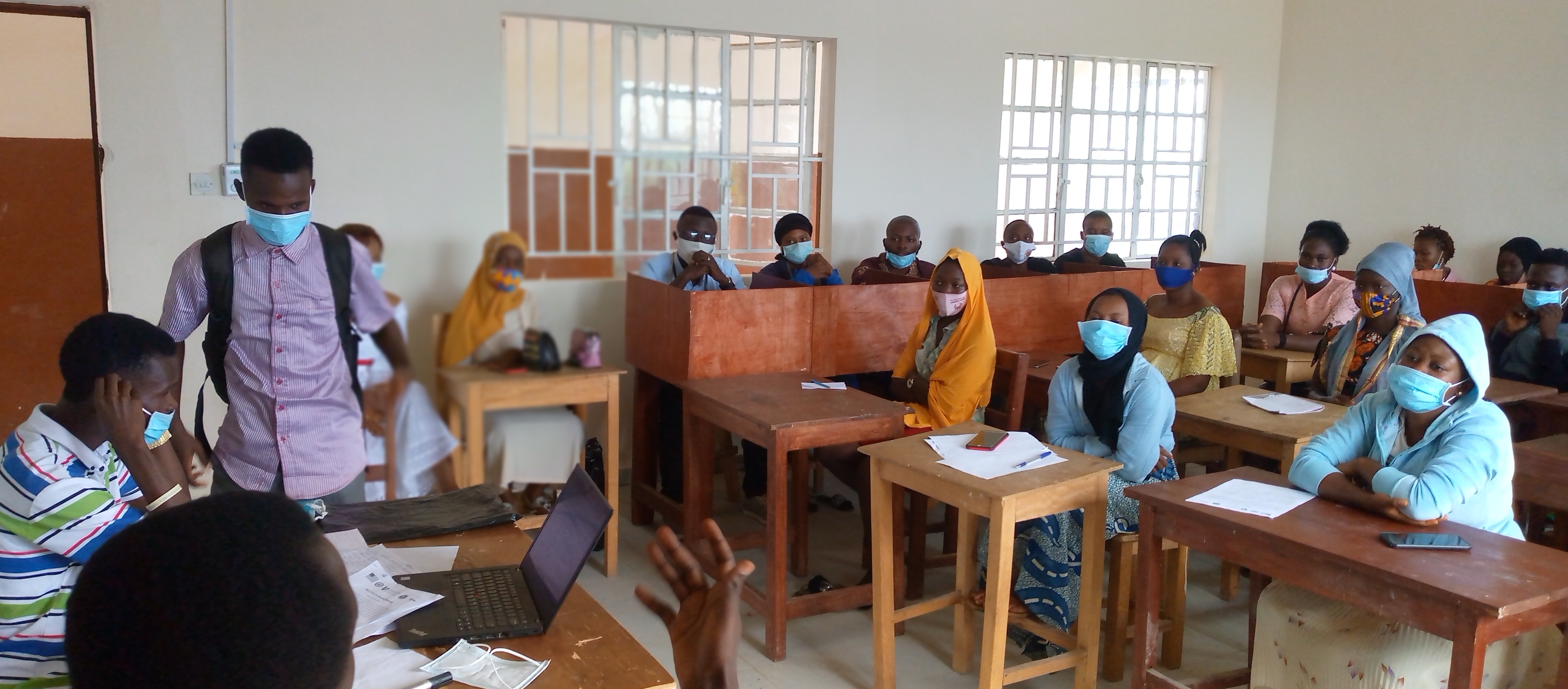 a large group of students wearing masks sit in a classroom behind desks