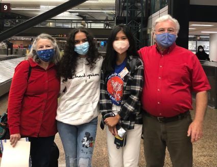 YES student, Felicia, standing with her host family at the airport. All four people are wearing masks.