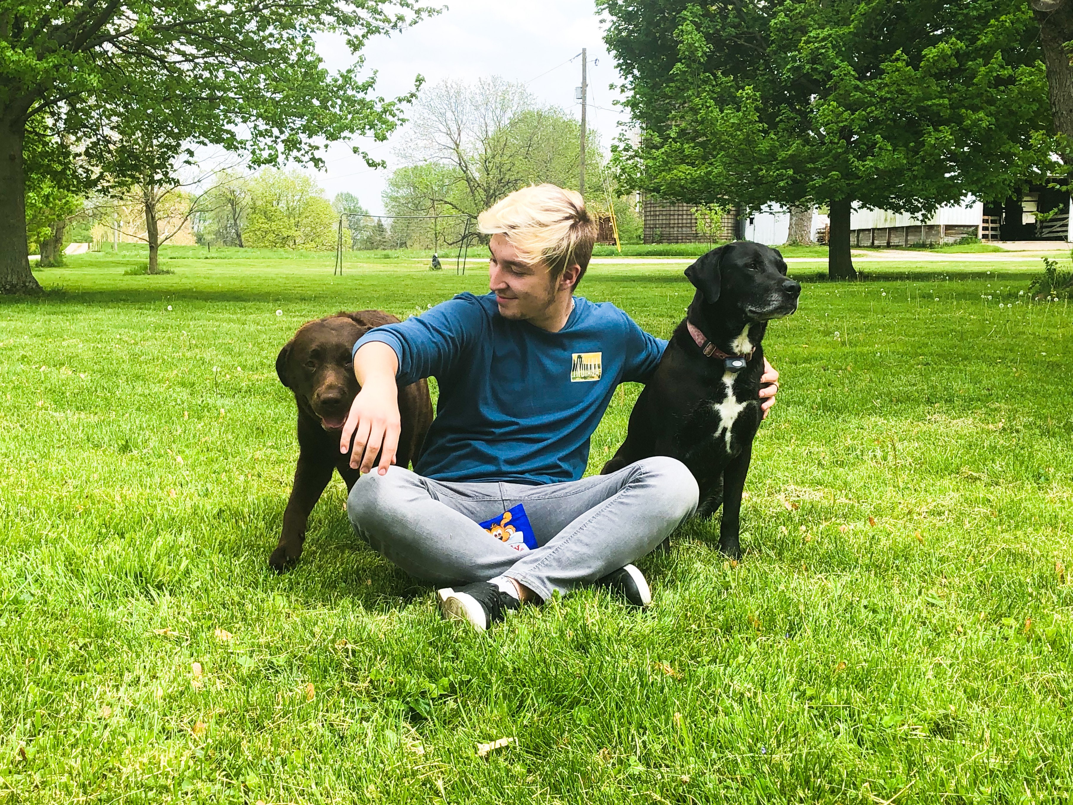 Lavdrim Sisting Next To Two Dogs On The Grass 2