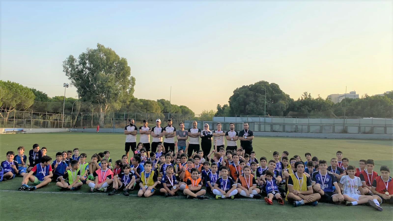 A wide photo of the large group of participants and coaches posing on the soccer field