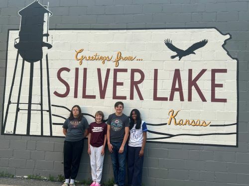 Abbiramyy with her host siblings in front of a sign saying Greetings from Silver Lake, Kansas