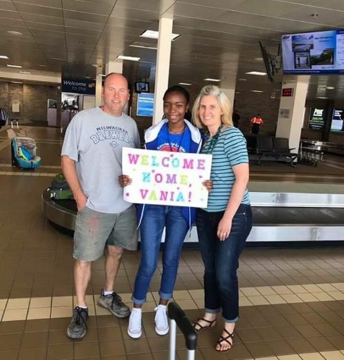 Vania and her host parents at the airport holding a Welcome Home sign