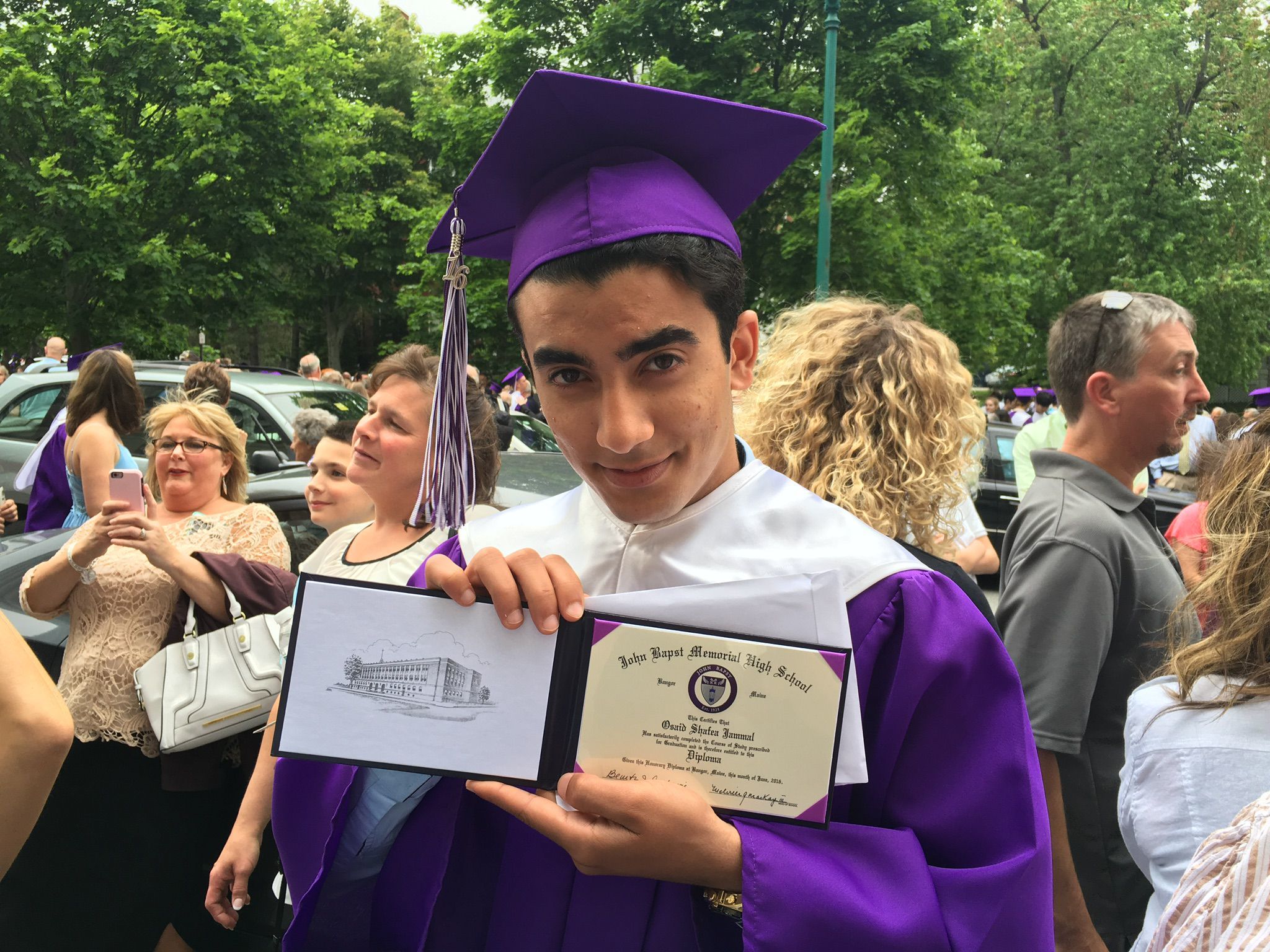 Osaid holding his high school certificate while wearing graduation cap and gown