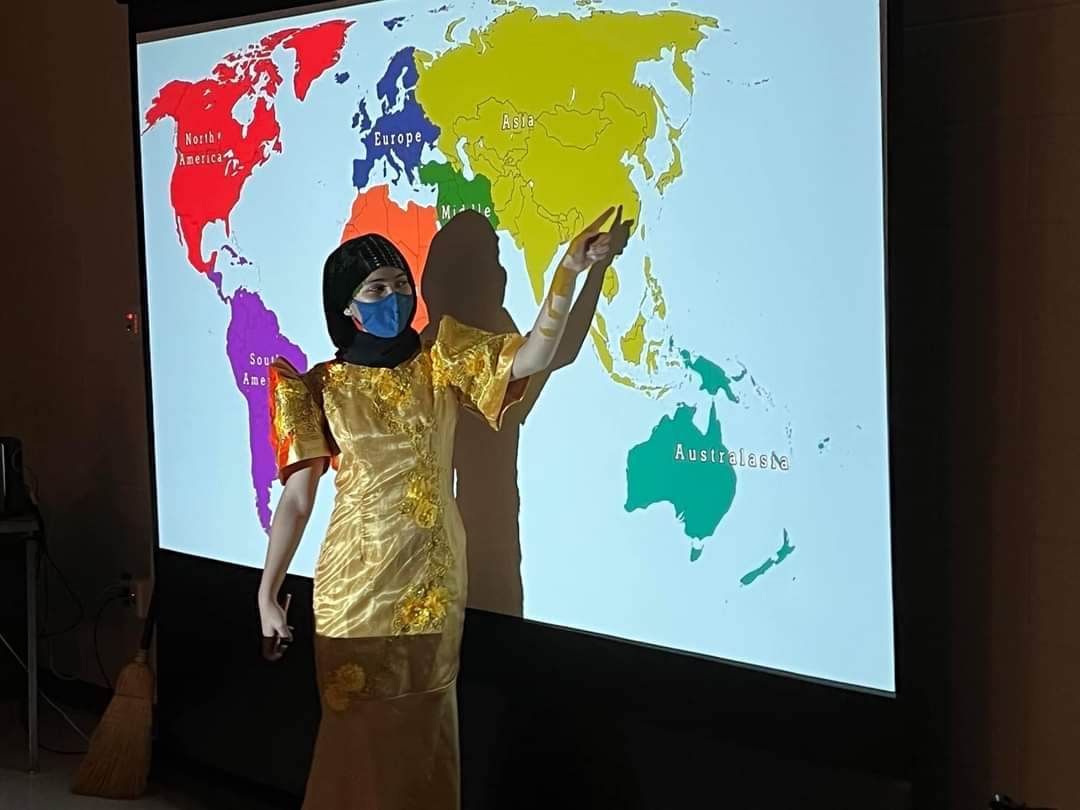 Hanafia points out where the Philippines is on a map while wearing traditional attire
