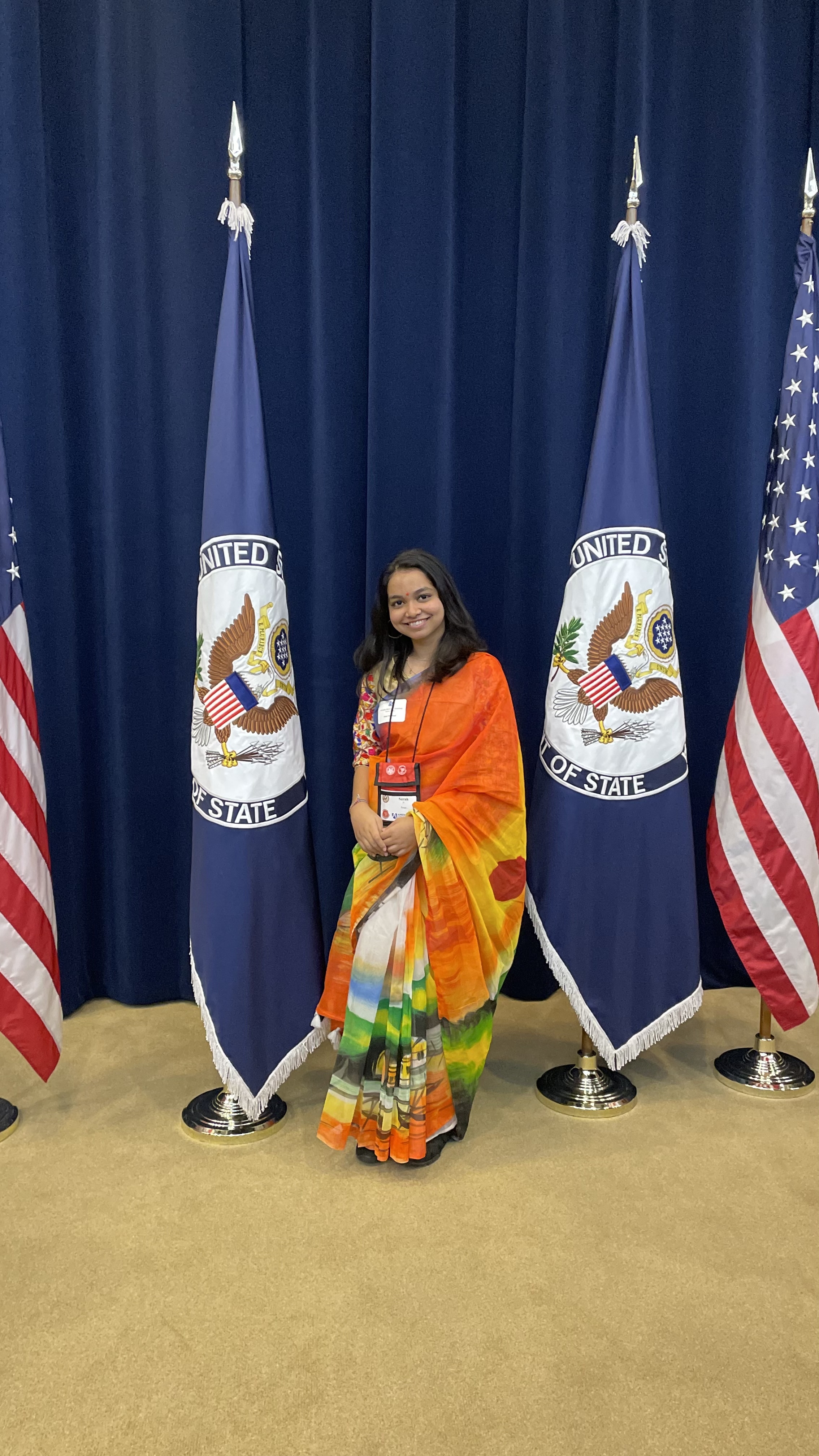 Photo Of Student In Traditional Dress Posing Between Congressional Flags Jpeg