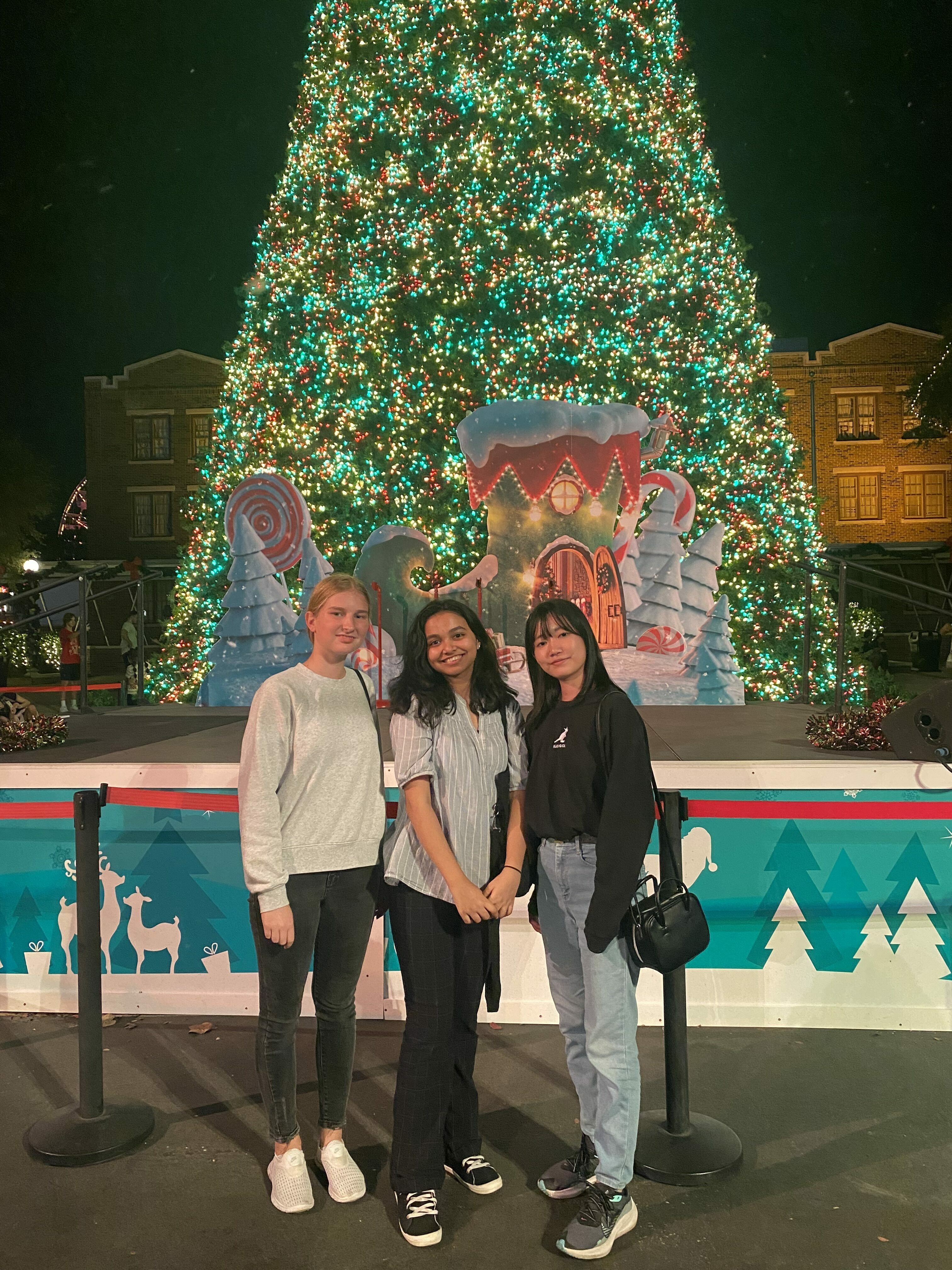 Photo Of Three Students Posing In Front Of Christmas Tree