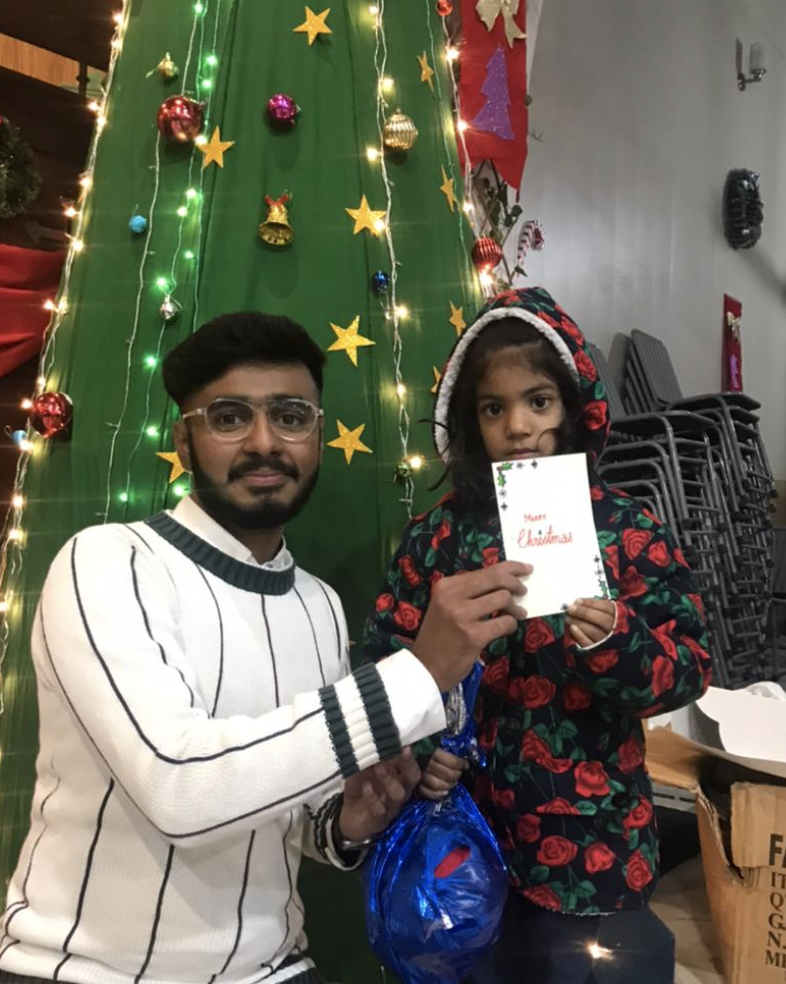 Husnain standing in front of a Christmas tree with a young girl.