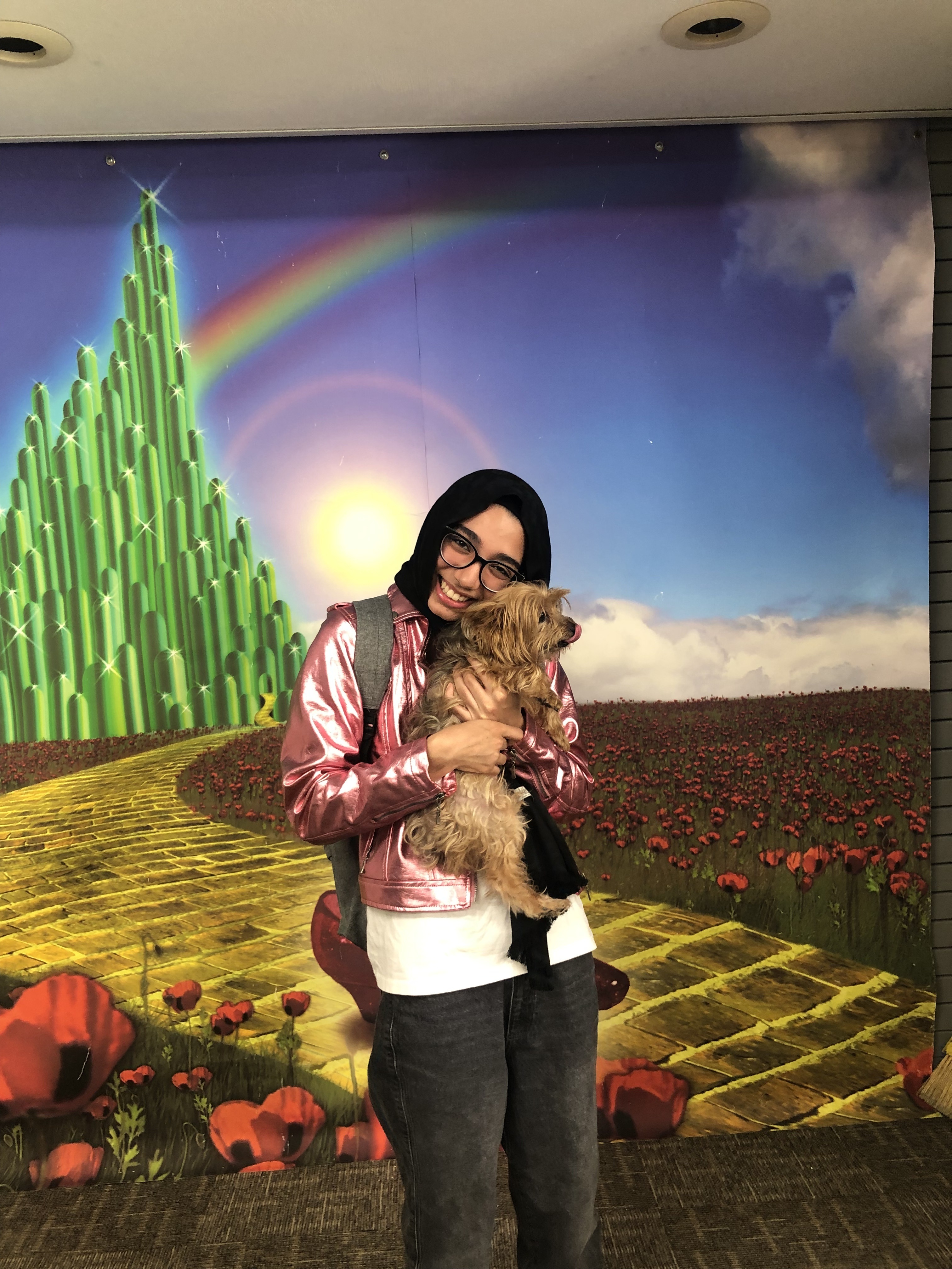 Sidrah holding a small brown dog in front of a backdrop from the Wizard of Oz