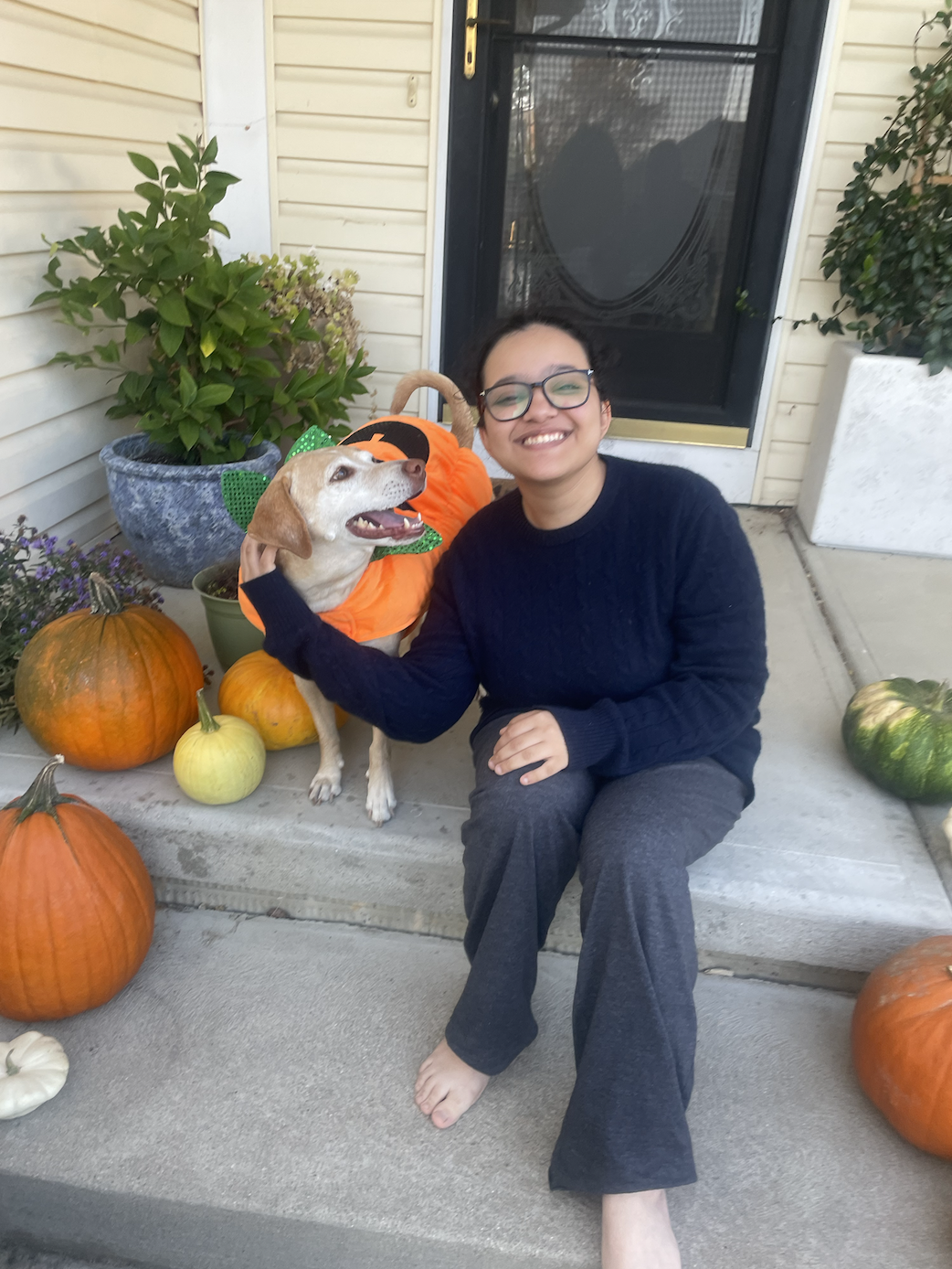 Student Poses On Front Porch With A Dog Wearing A Costume