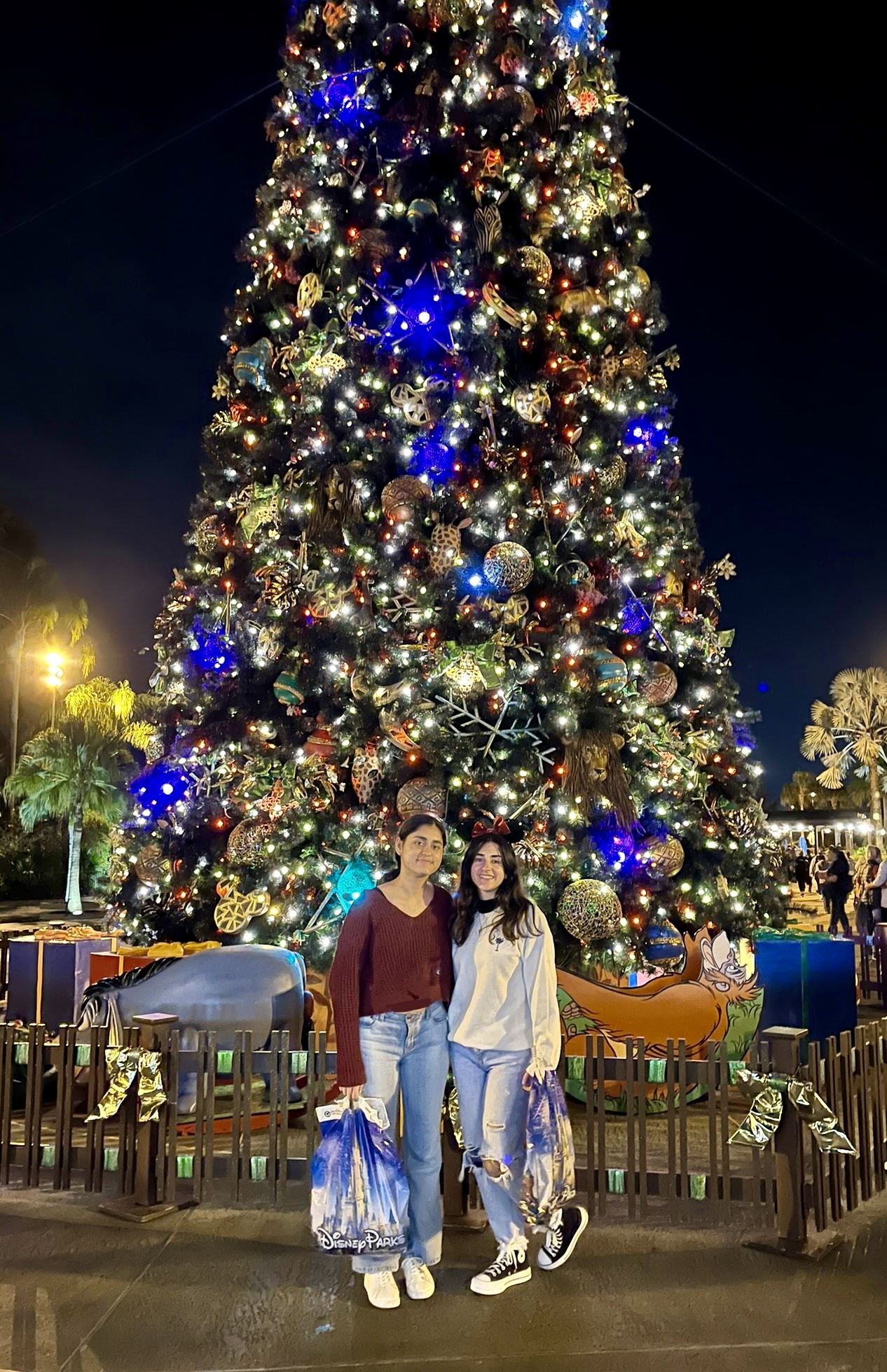 Two girls smiling in front of an enormous outdoor Christmas tree