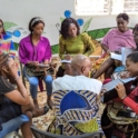 A group of participants sits in a circle discussing ideas and taking notes with one working on a laptop The setting features colorful murals and a banner