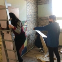 A student steps down from a ladder as another student looks at the design plans for a wall in the mental health club room. 