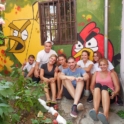 Alumni sit against a colorful wall with a mural of angry birds
