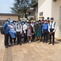 A large group of alumni and youth stand outside a school and smile