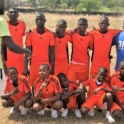 A soccer team in Tanzania wearing red uniforms, a coach in an IRIS tshirt