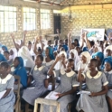 A facilitator leading a session with a big group of female students seated rising their hands and laughing